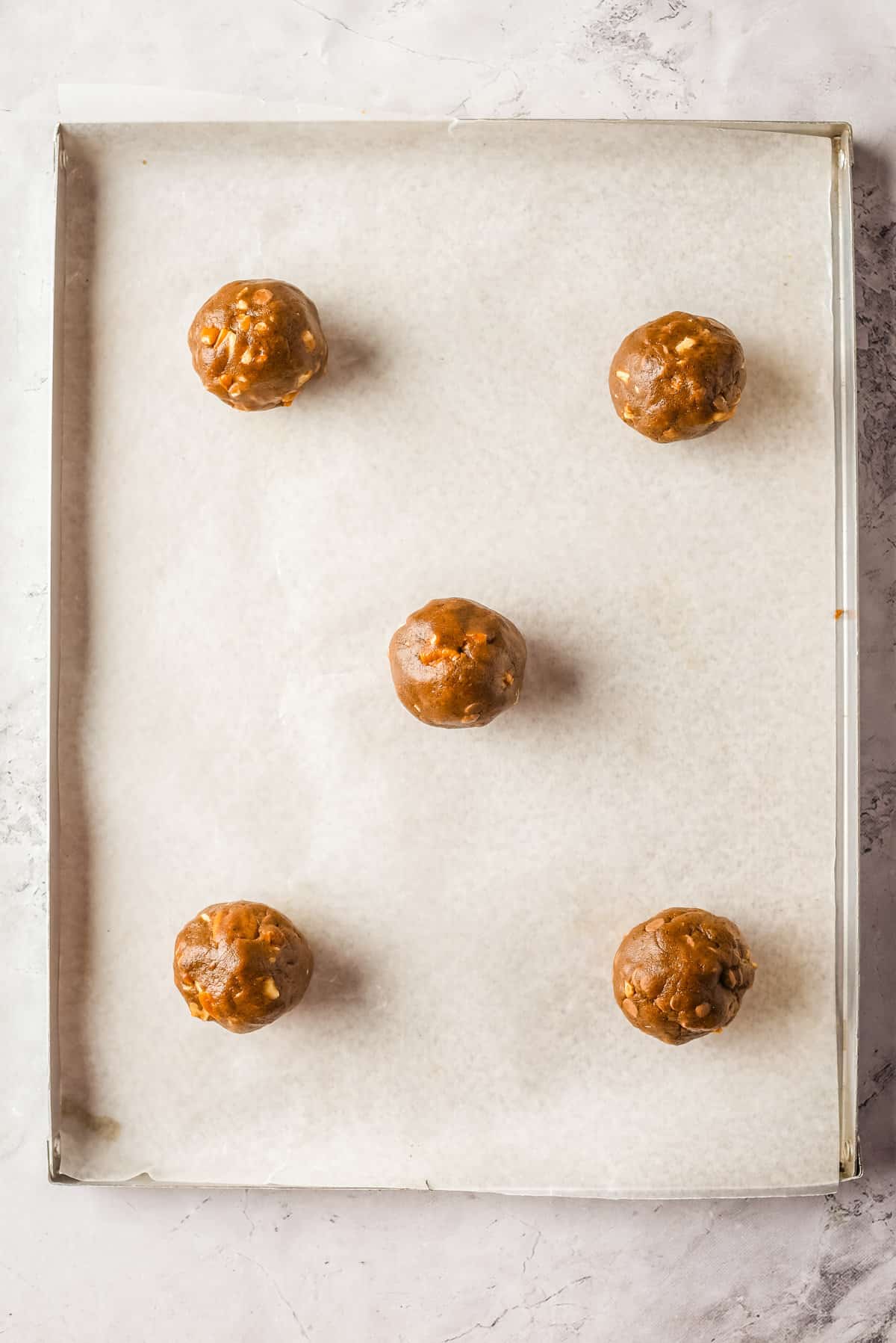 Overhead view of pecan chocolate chip cookie dough balls on a parchment-lined baking sheet. 