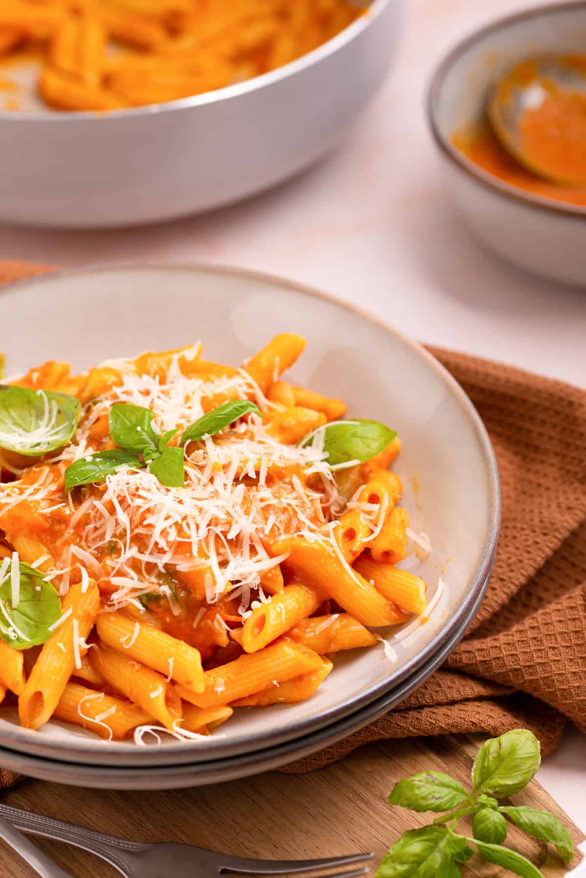 Close up view of penne pomodoro on a white plate, with basil leaves and cheese as garnish. 