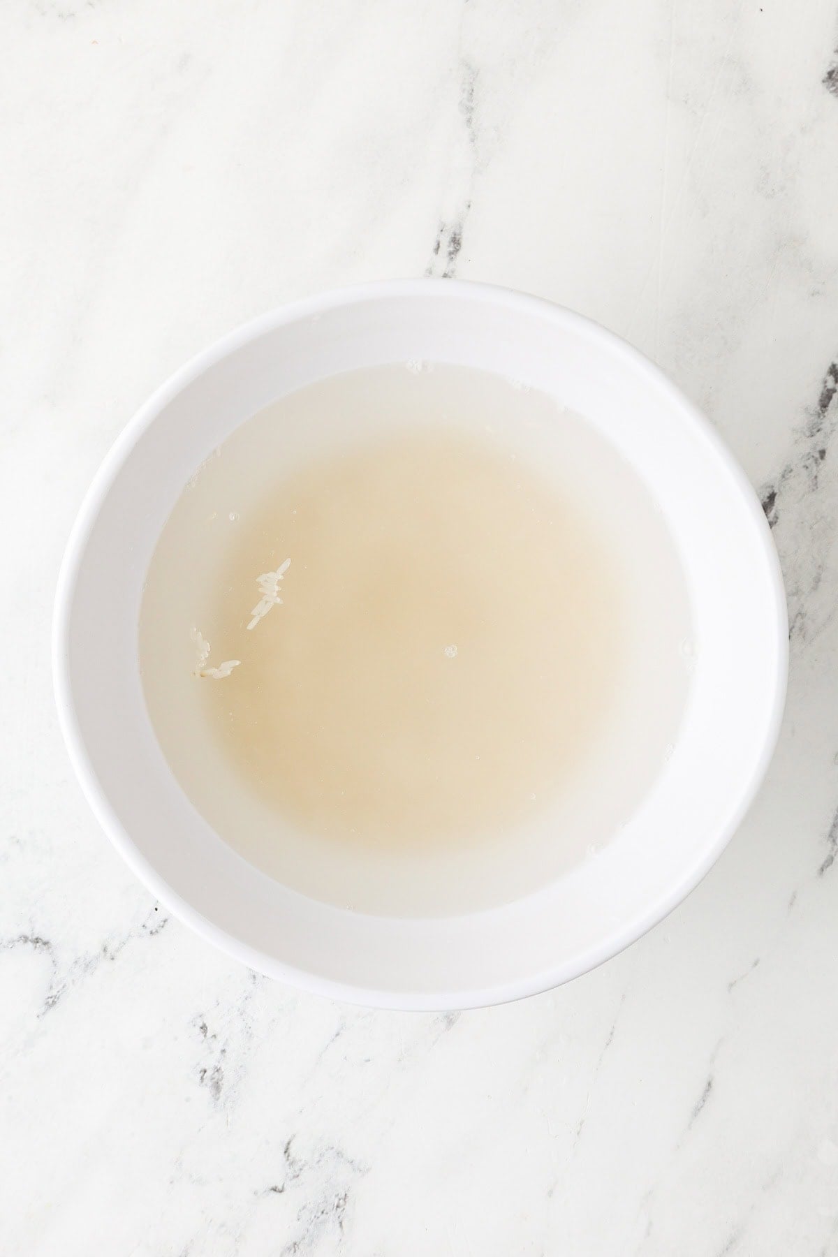 An overhead image of jasmine rice soaked in a bowl with water.