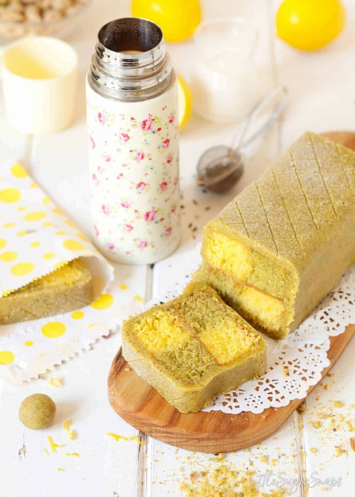 A straight view of the Pistachio Lemon Battenberg Cake with Pistachio Marzipan and pistachio and lemons in the background.