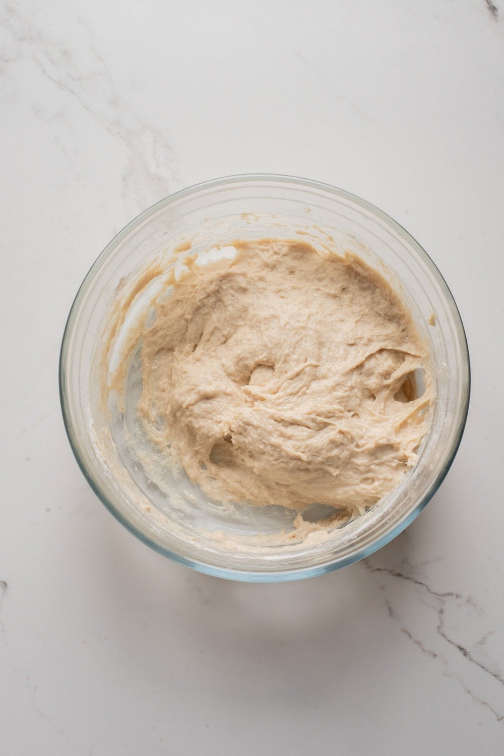 Thick, sticky puff puff batter in a glass bowl before rising.
