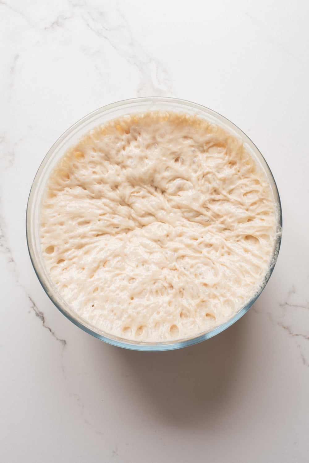 Risen puff puff batter with a bubbly surface in a glass bowl.