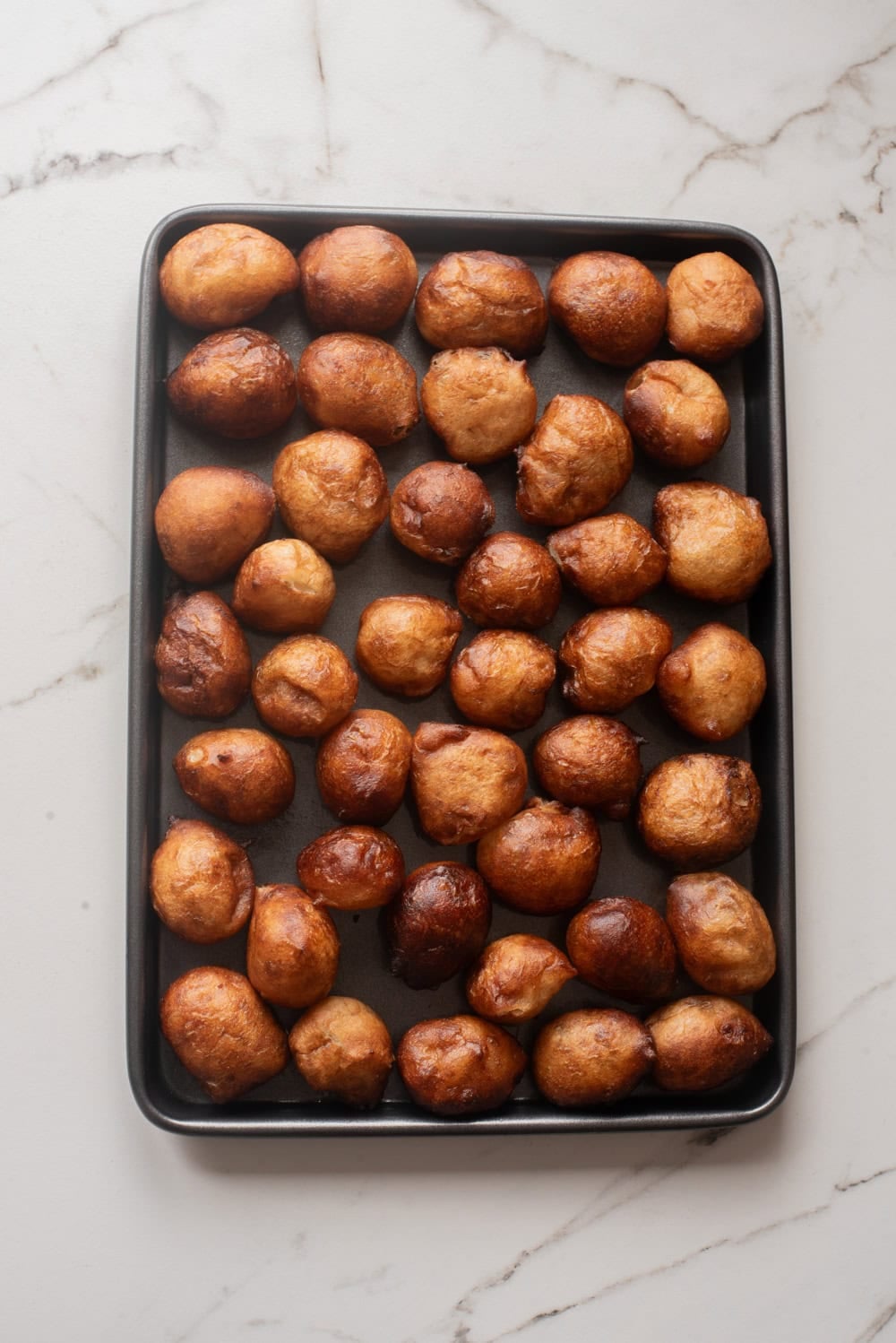 Golden-brown Nigerian puff puff arranged on a black baking tray after frying.