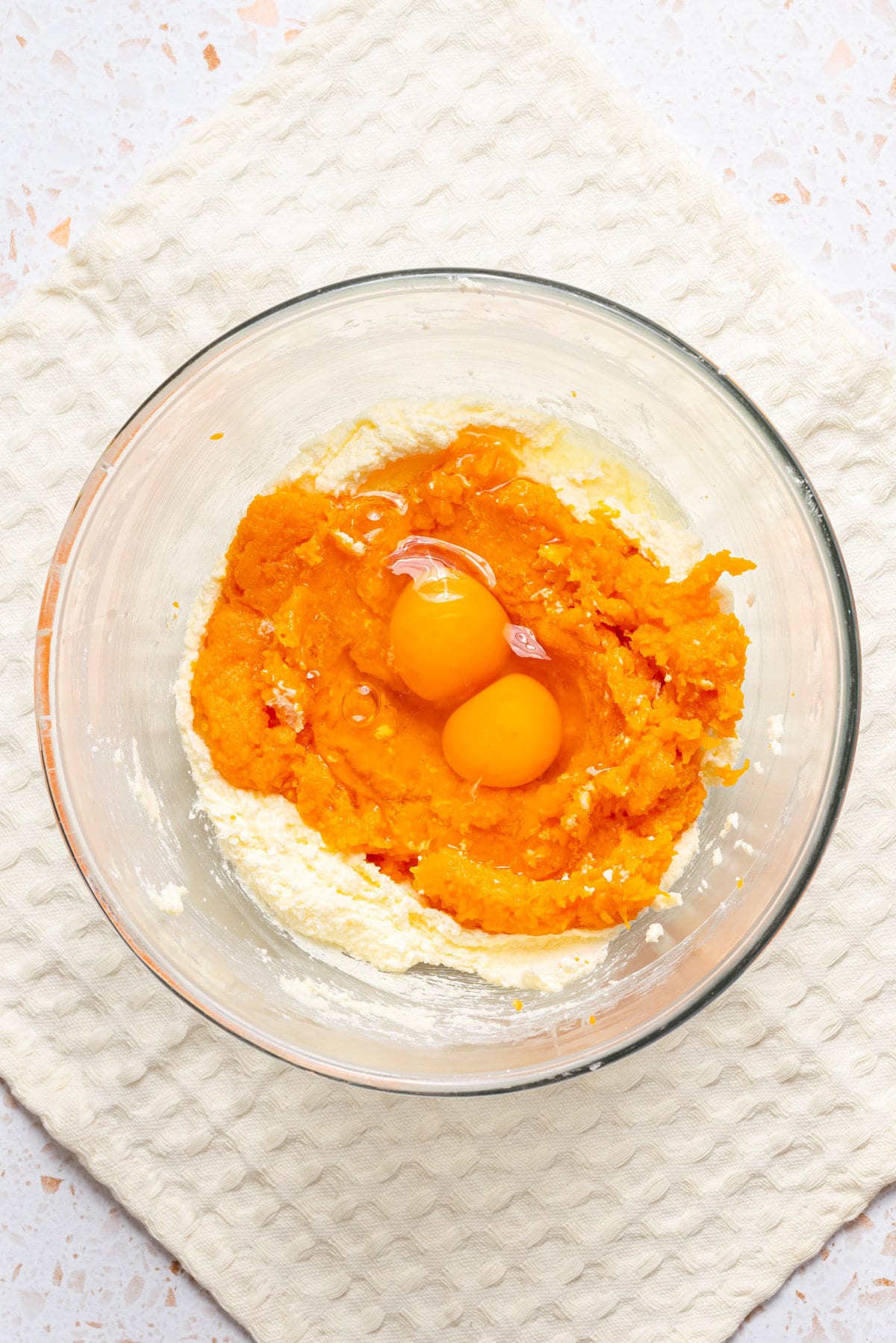 An image of pumpkin puree and eggs being added to a mixing bowl.