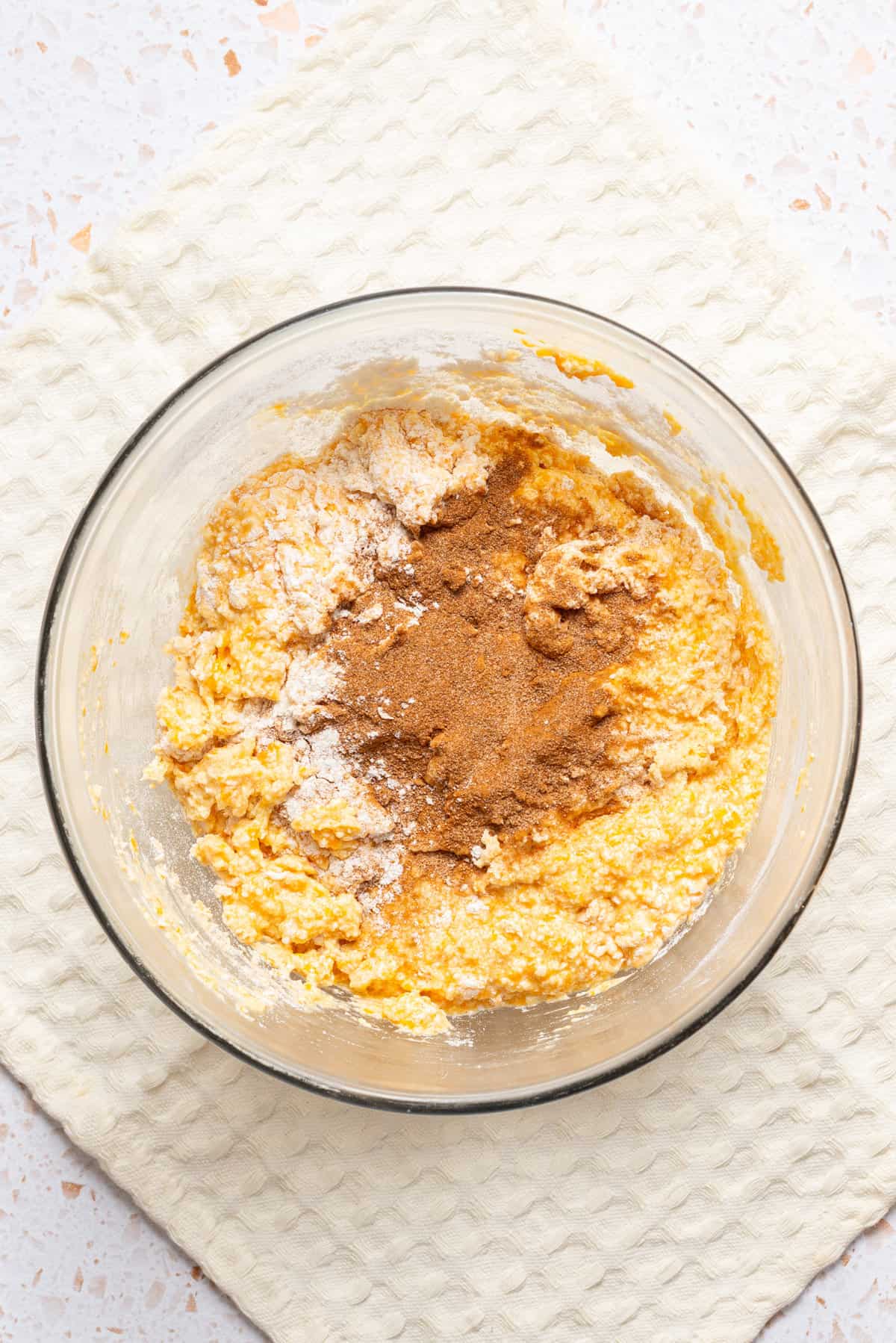 An image of flour, baking powder, and pumpkin spice being added to a mixing bowl.