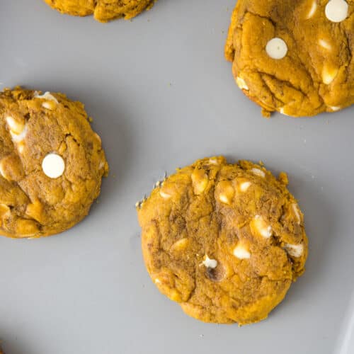 Overhead view of pumpkin white chocolate chip cookies on a gray baking sheet.