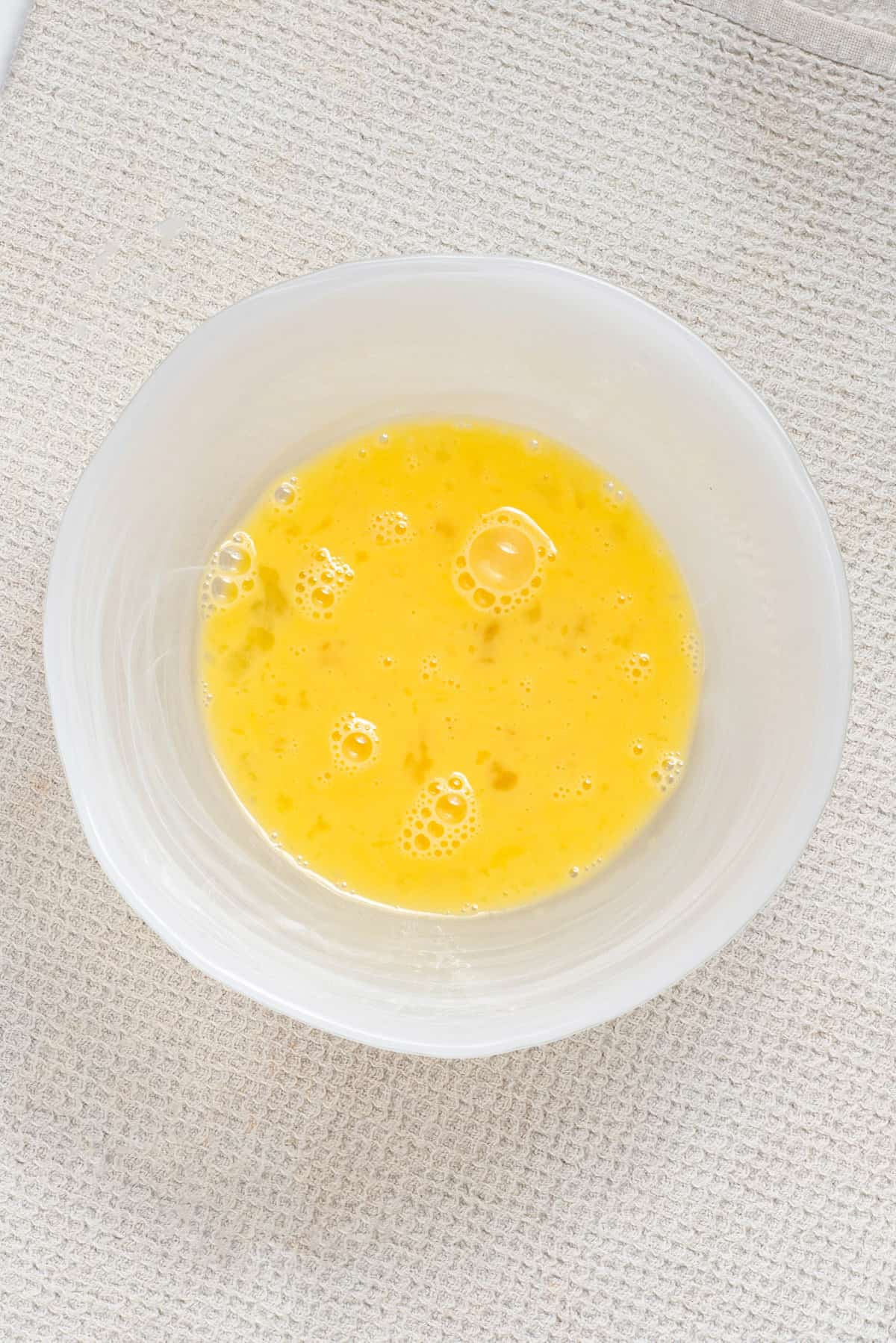 Overhead view of whisked eggs in a white bowl.