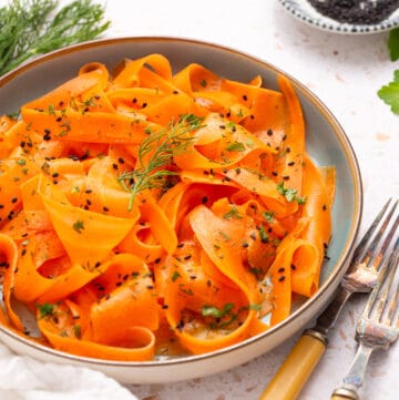 An image of raw carrot salad on a serving plate with two forks on the side.