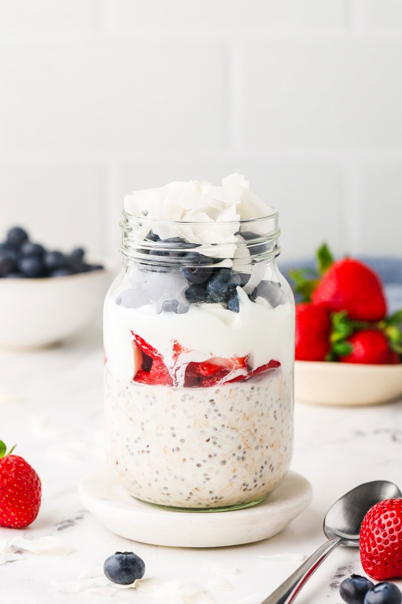 Layered Red, White & Blue Overnight Oats with strawberries, Greek yogurt, blueberries, and shredded coconut ready to serve.