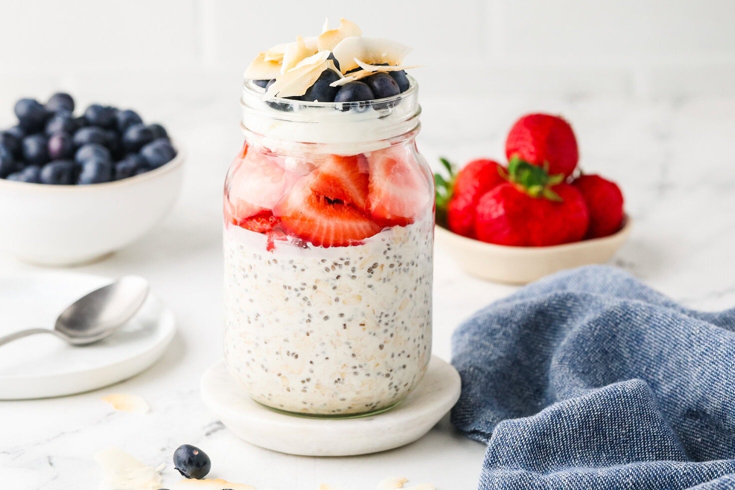 Red, White & Blue Overnight Oats served in a mason jar with fresh strawberries and blueberries on a marble countertop.