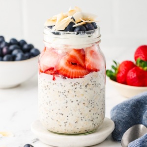 Jar of Red, White & Blue Overnight Oats layered with strawberries, Greek yogurt, blueberries, and shredded coconut.