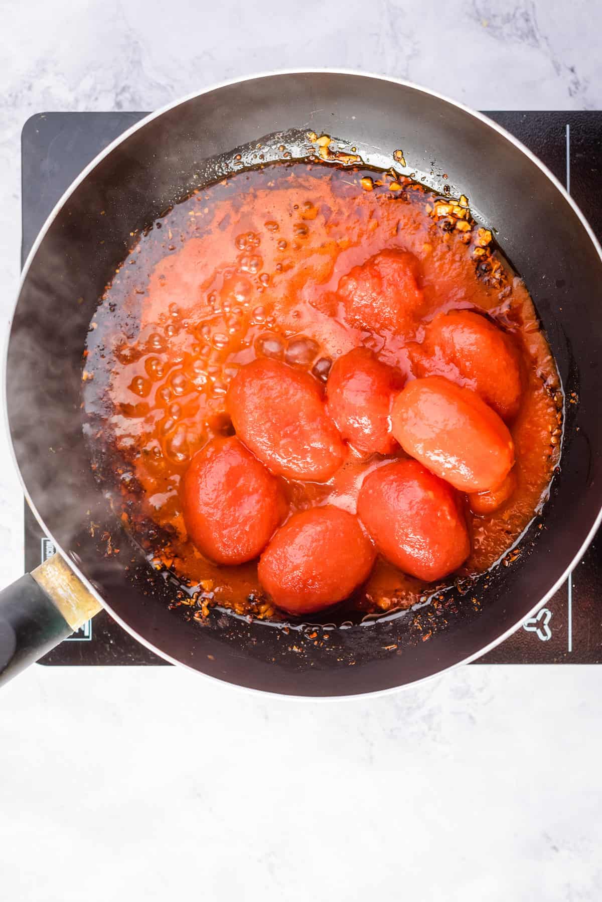 Overhead view of peeled tomatoes stirred in a large skillet pan.