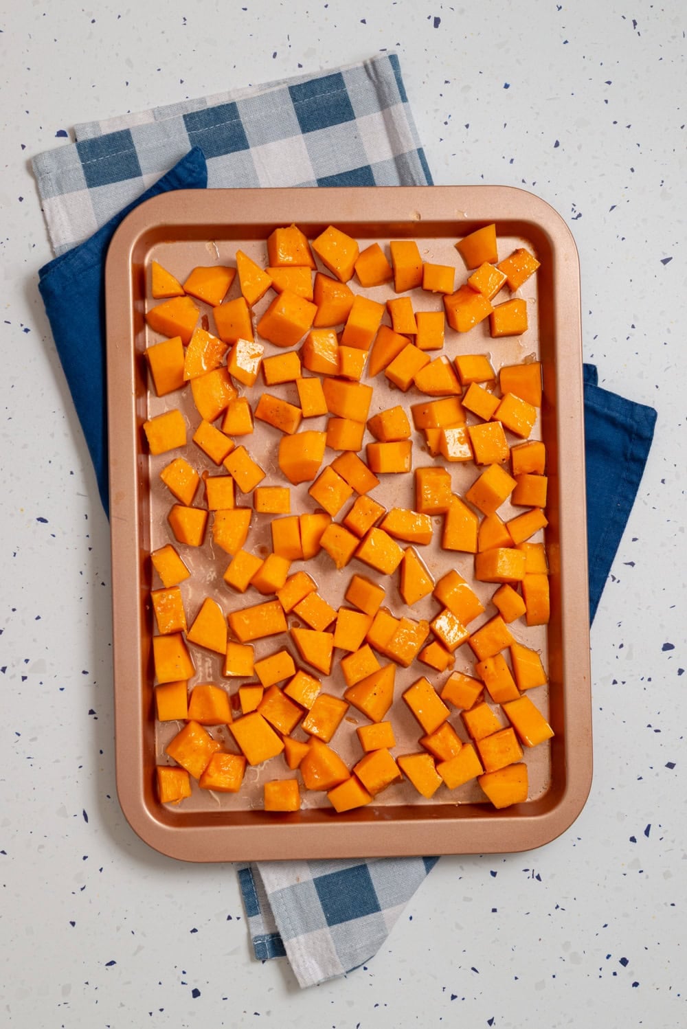 Cubed butternut squash spread in an even layer on a sheet pan before roasting.
