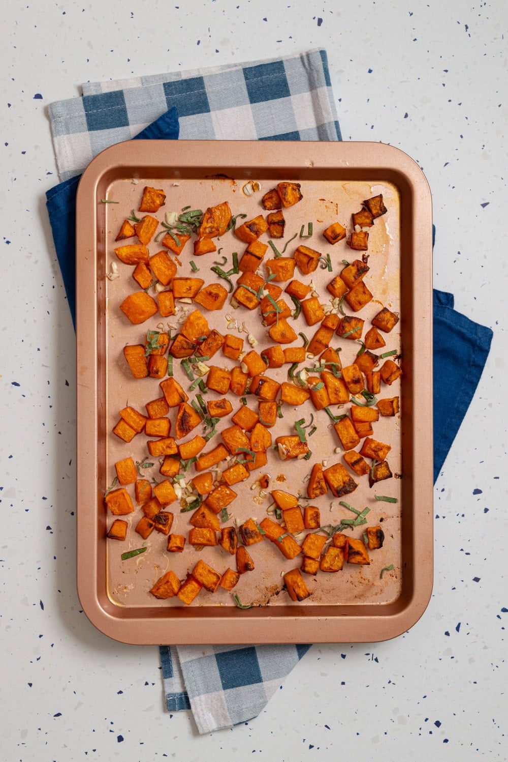 Roasted butternut squash cubes with garlic and fresh sage scattered across the sheet pan.