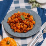 Roasted butternut squash cubes with deeply browned edges and fresh sage on a blue plate.