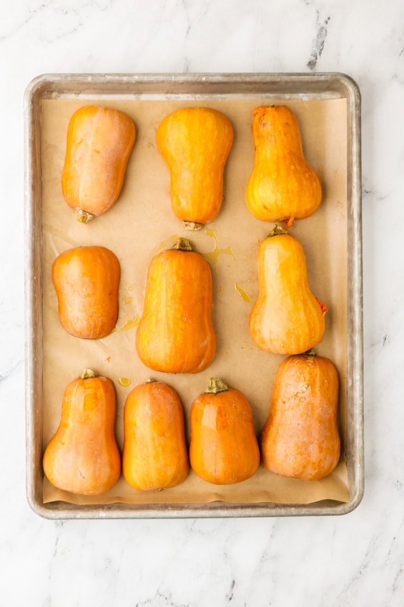 Honeynut squash halves roasting cut-side down on a baking sheet.