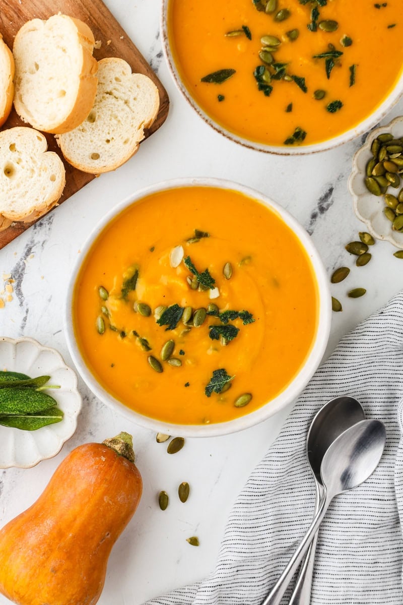Two bowls of roasted honeynut squash soup topped with crispy sage and pepitas.