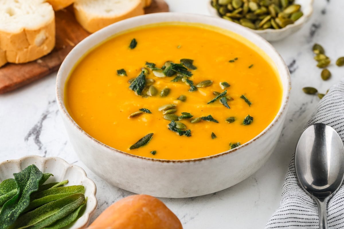 Roasted honeynut squash soup topped with crispy sage and pepitas, served with sliced bread.