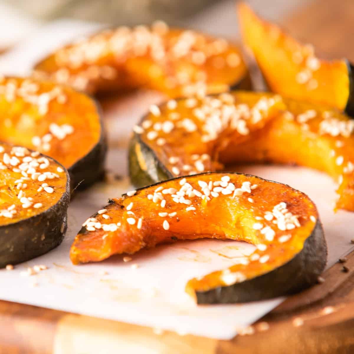 Close up of roasted kabocha squash with sesame seed garnish on a parchment paper on wooden platter.