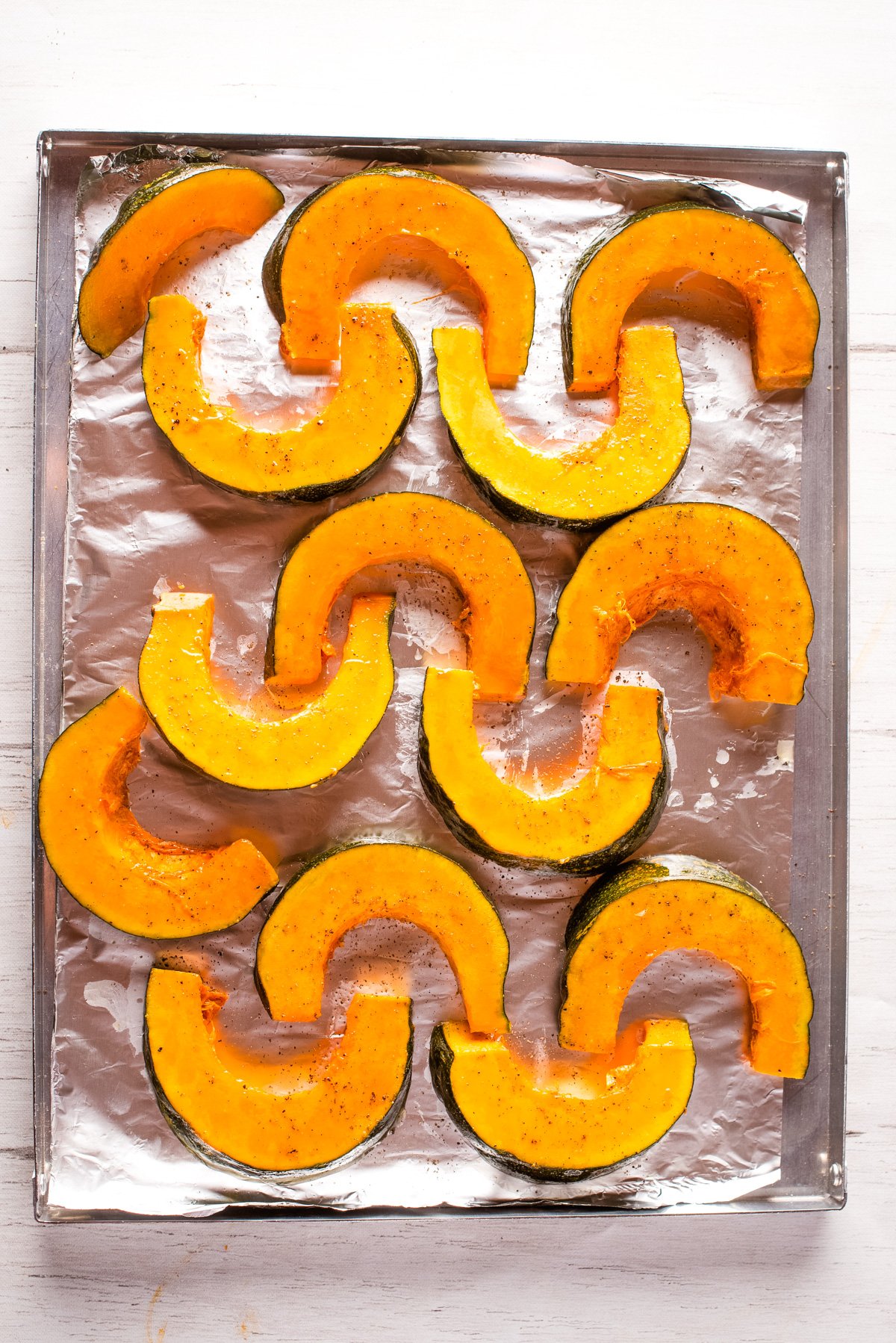 Overhead view of kabocha squash slices on a baking sheet.