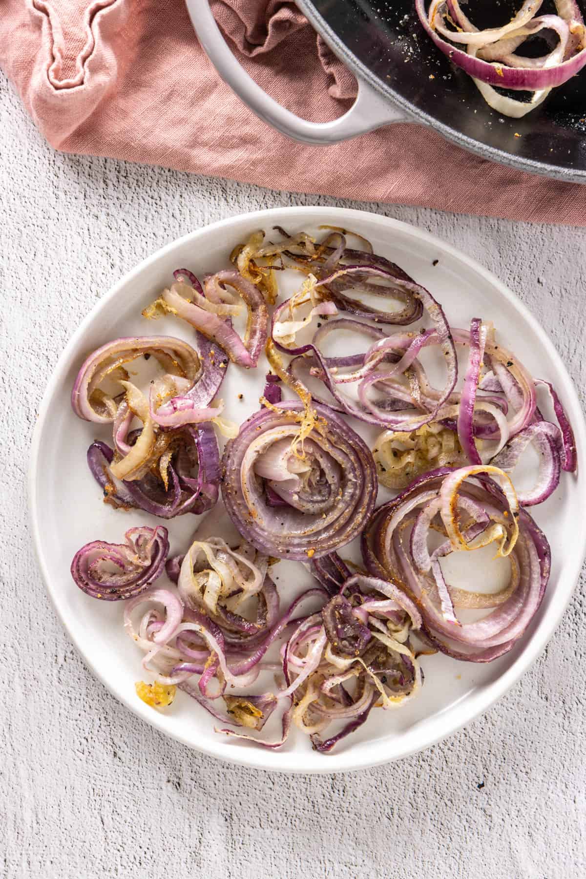 Close up of plate of roasted red onions with skillet in the background