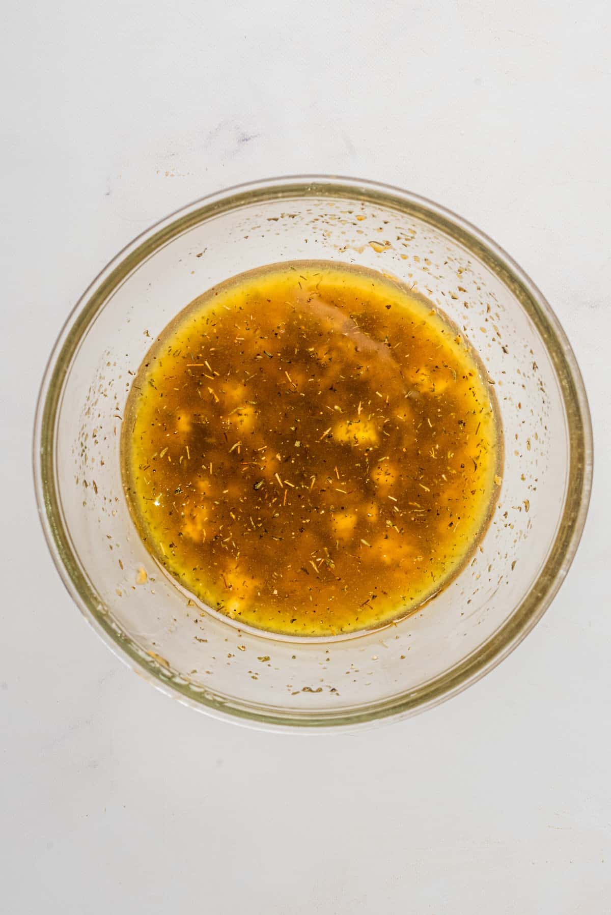An overhead image of a mixture of oil, vinegar, sweetener of choice, dijon mustard, minced garlic, thyme, salt, and pepper whisked together in a small bowl.