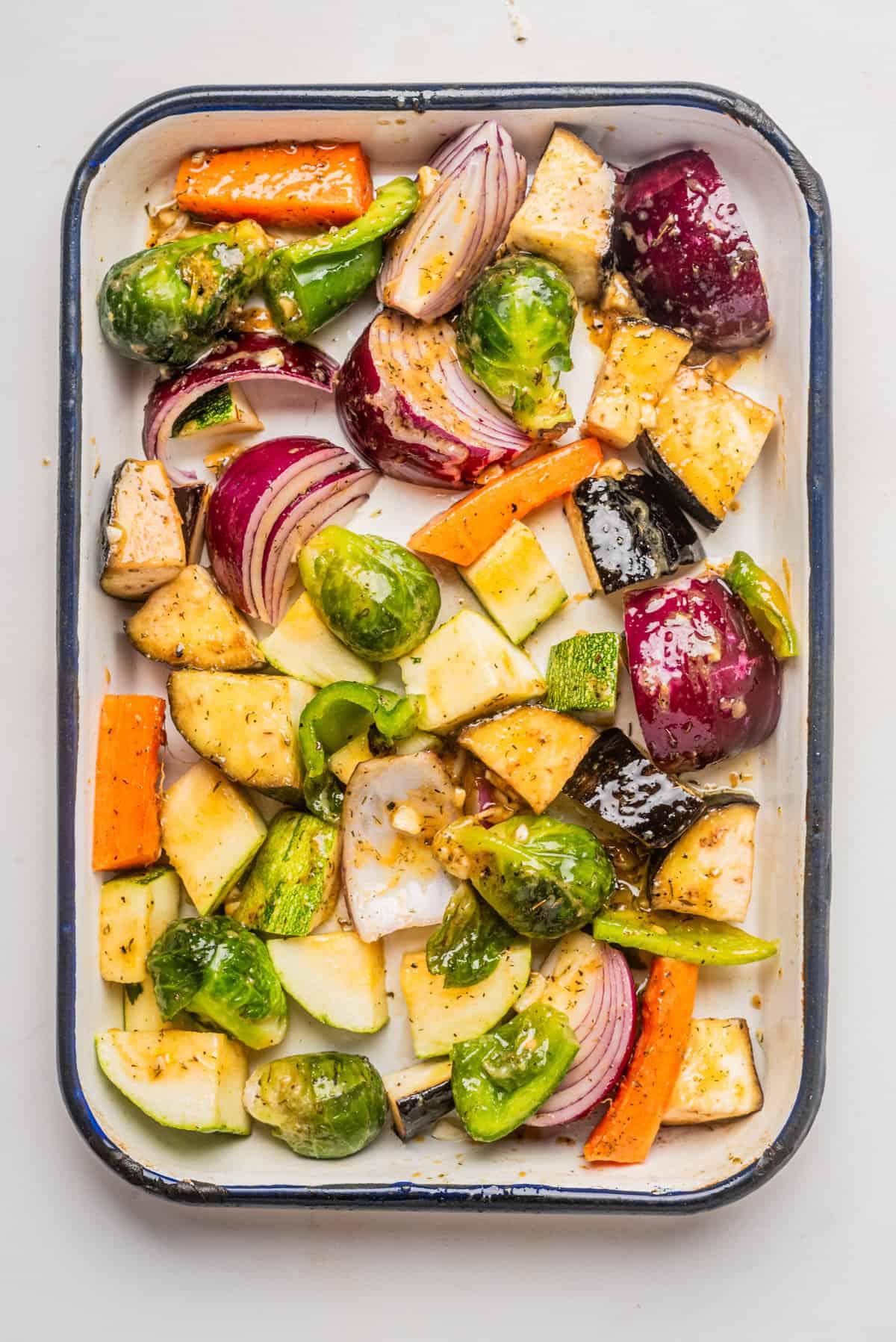 An overhead image of chopped vegetables brushed with vinegar dressing on a baking dish..