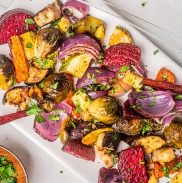 An overhead image of roasted vegetable salad on a serving dish. with the dressing on the side.