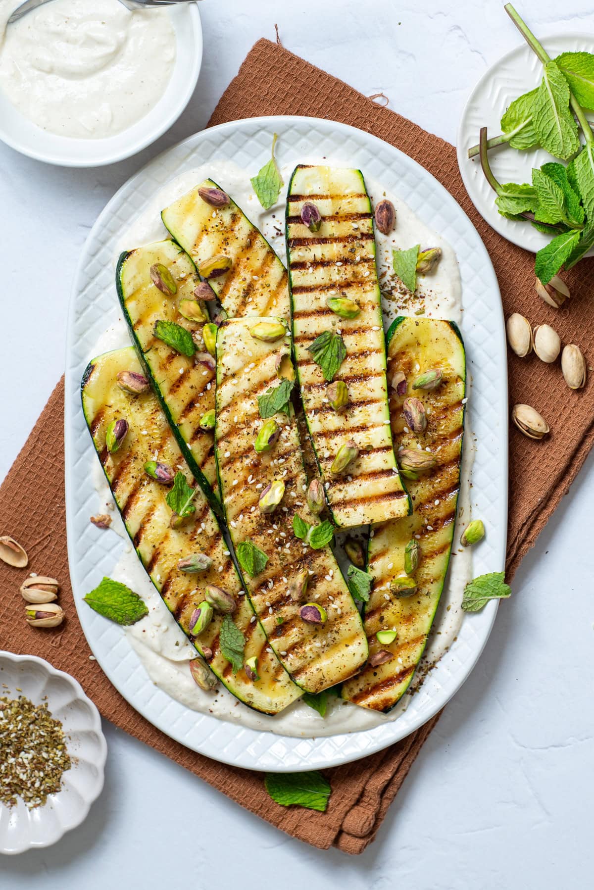 An overhead image of grilled zucchini with tahini sauce.