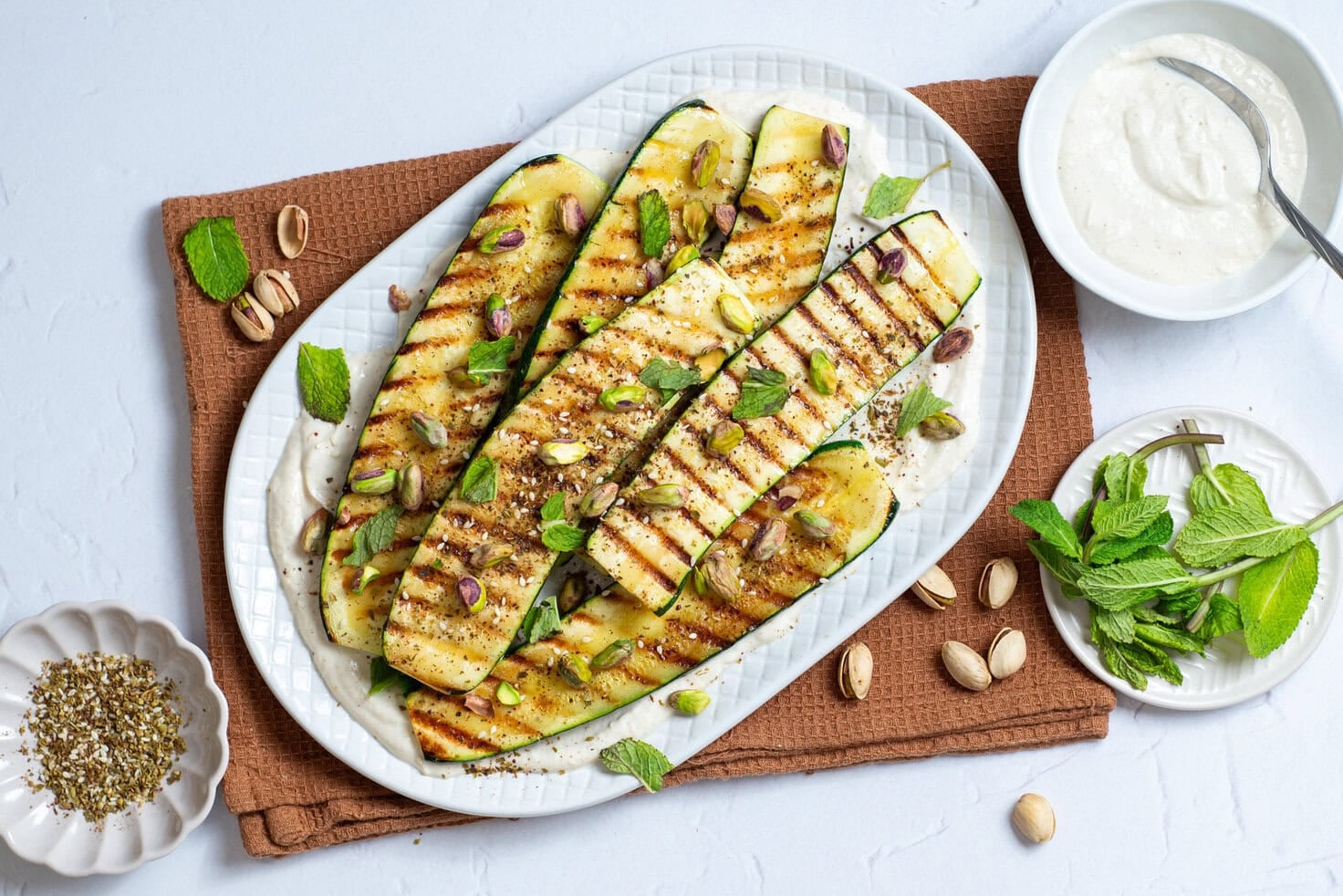 An overhead image of grilled zucchini with tahini sauce on the side.