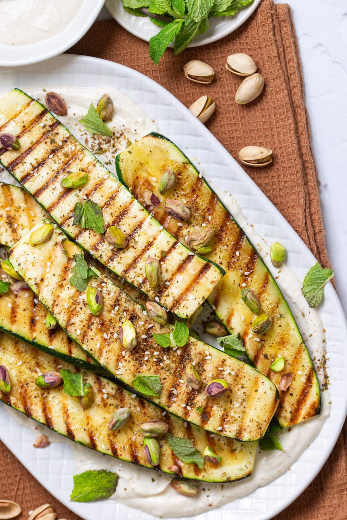 An overhead image of grilled zucchini with tahini sauce on the side.