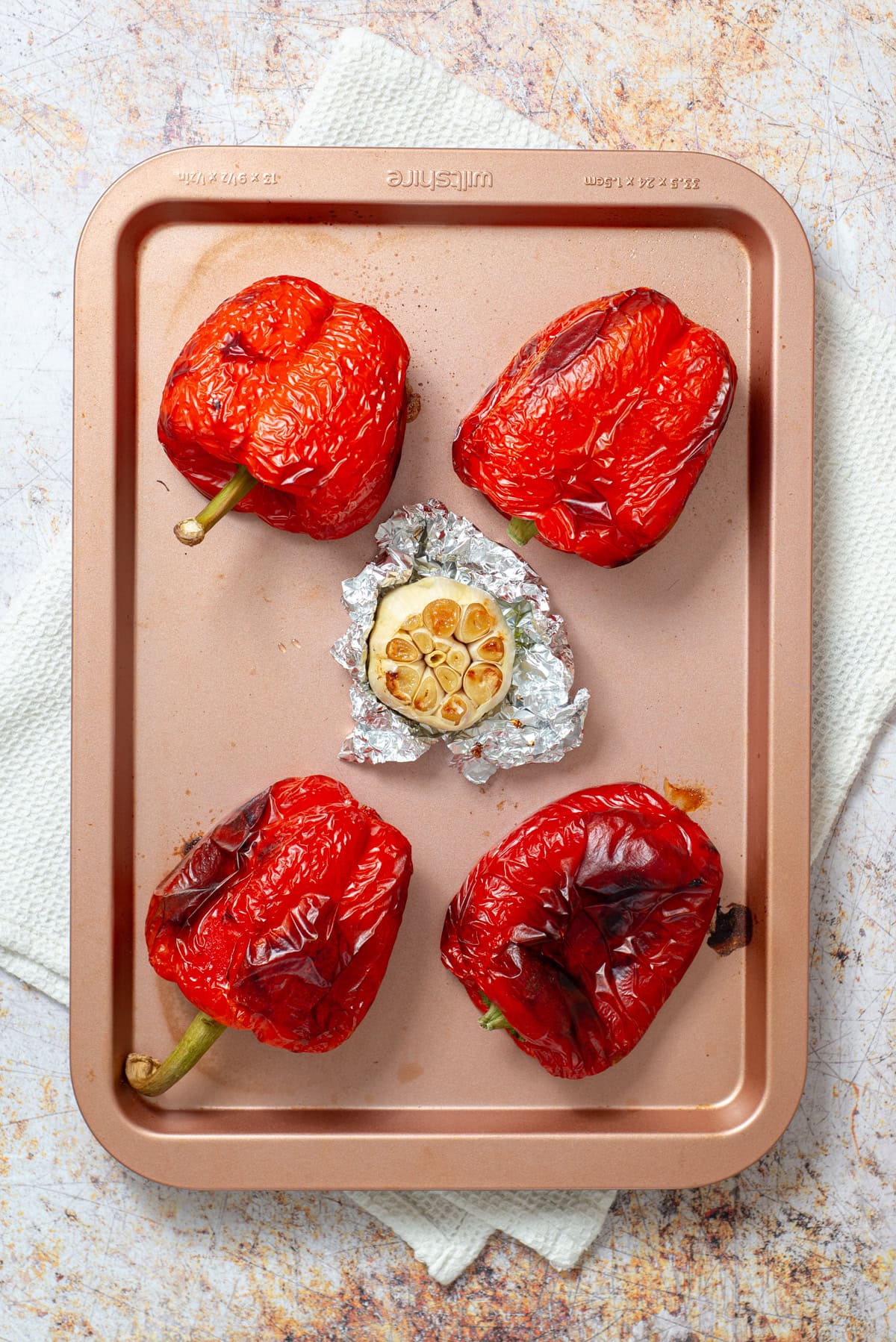Roasted red bell peppers and roasted garlic on a baking sheet.