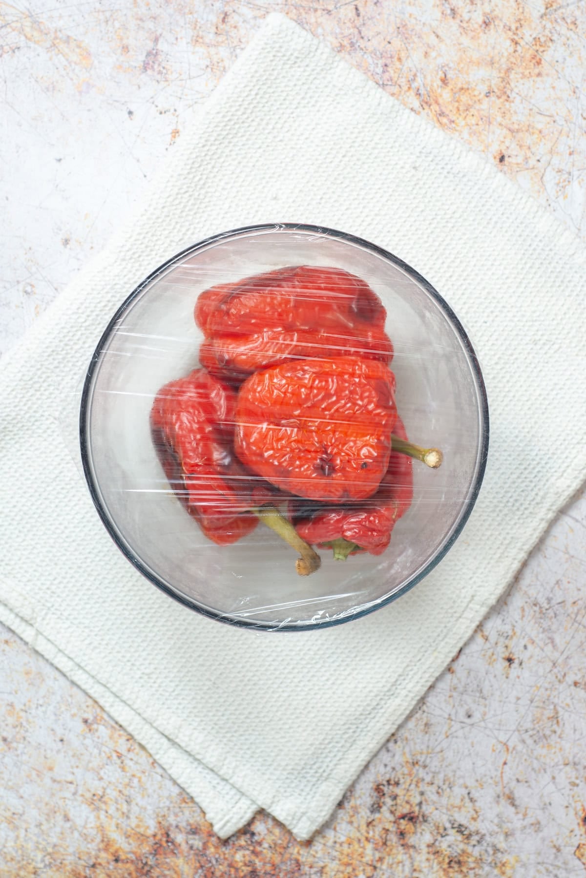Roasted red peppers steaming in a covered glass bowl.