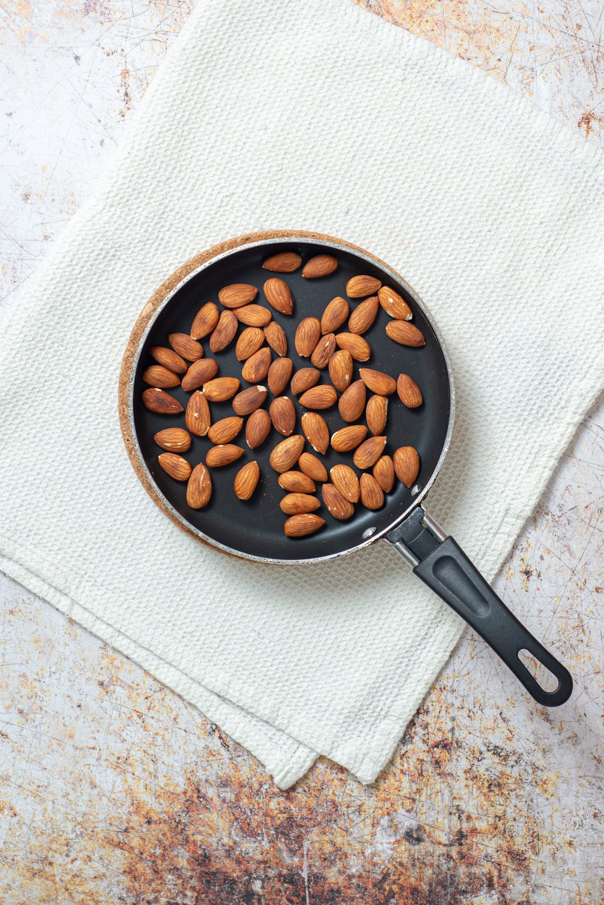 Raw almonds toasting in a skillet.