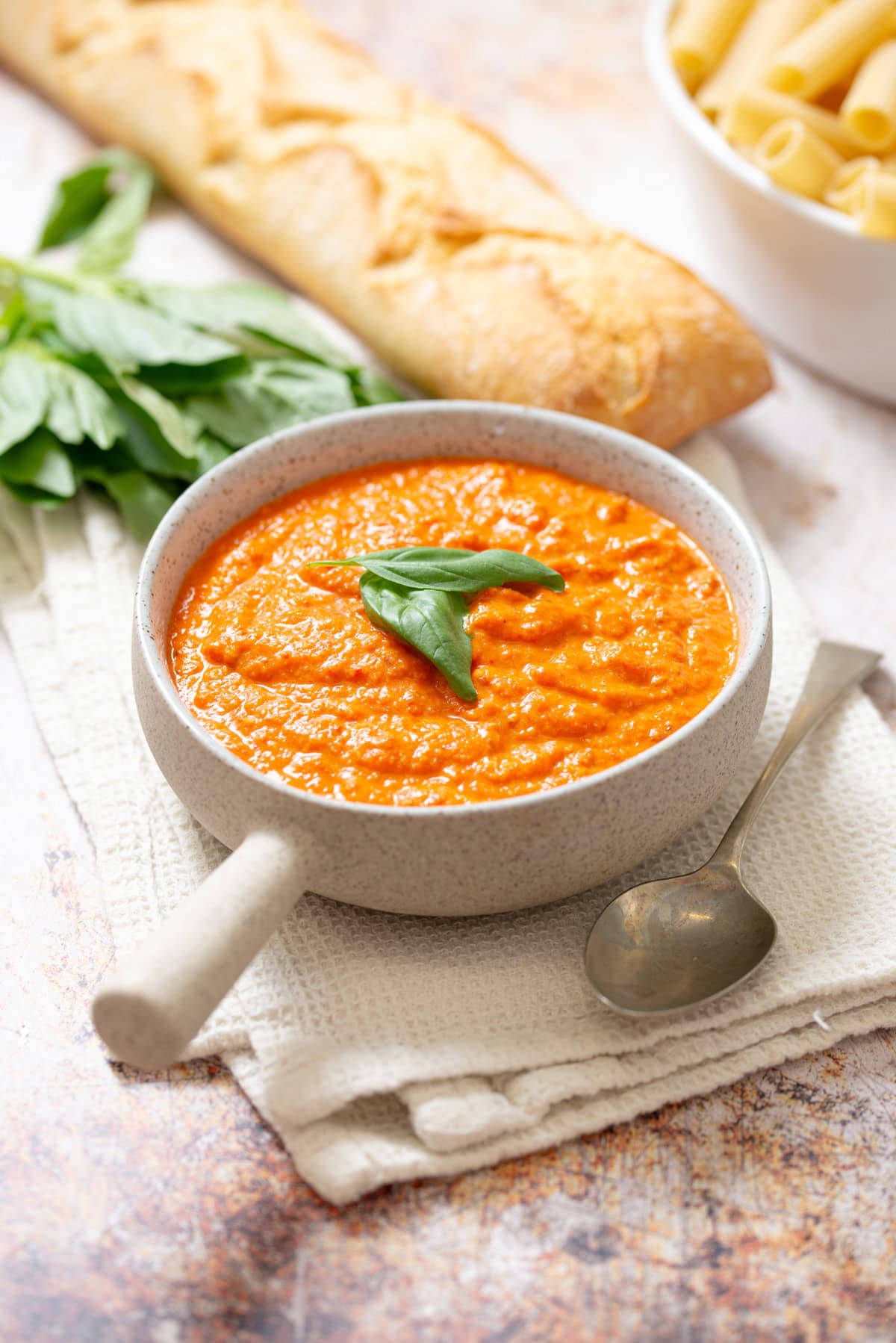 Homemade romesco sauce in a ceramic bowl with fresh basil, served with crusty bread.