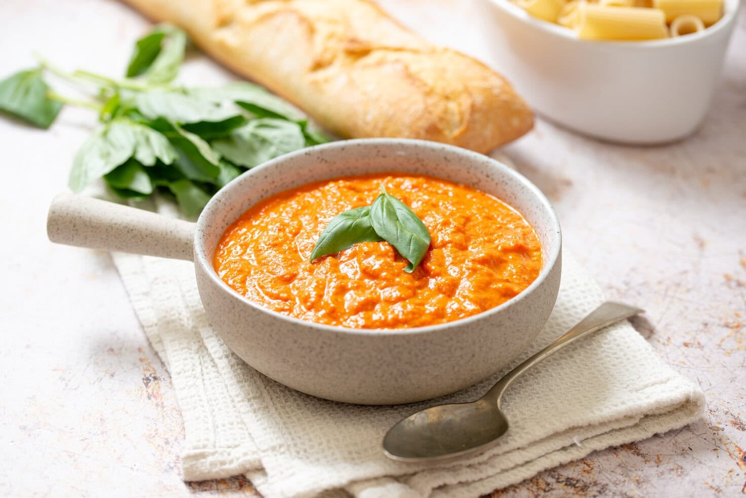 Homemade romesco sauce served in a bowl with basil, crusty bread, and fresh herbs.