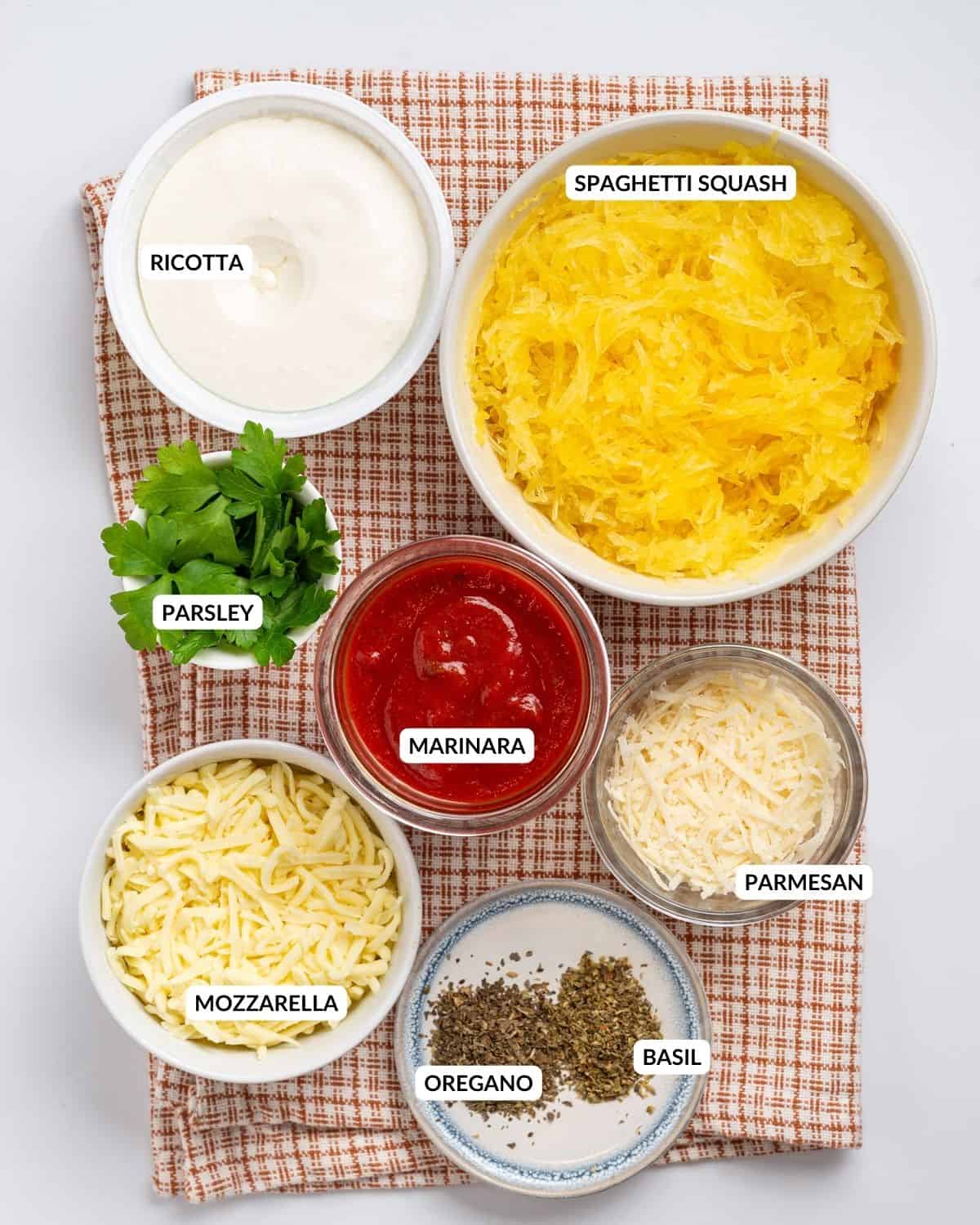 An overhead image of the ingredients of spaghetti squash lasagna laid out in separate containers with labels.