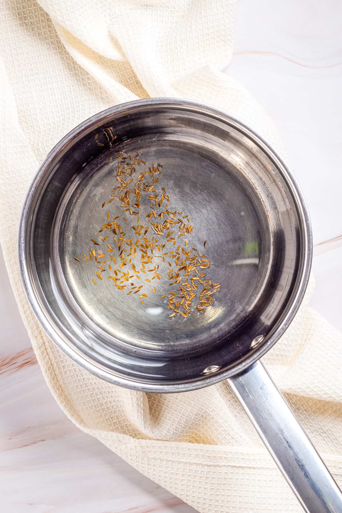 Overhead view of a pan with oil and cumin seeds. 