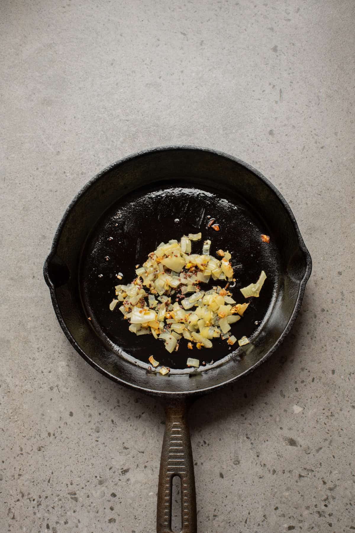 An overhead image of adding onions, ginger, and garlic after blooming the cumin seeds.