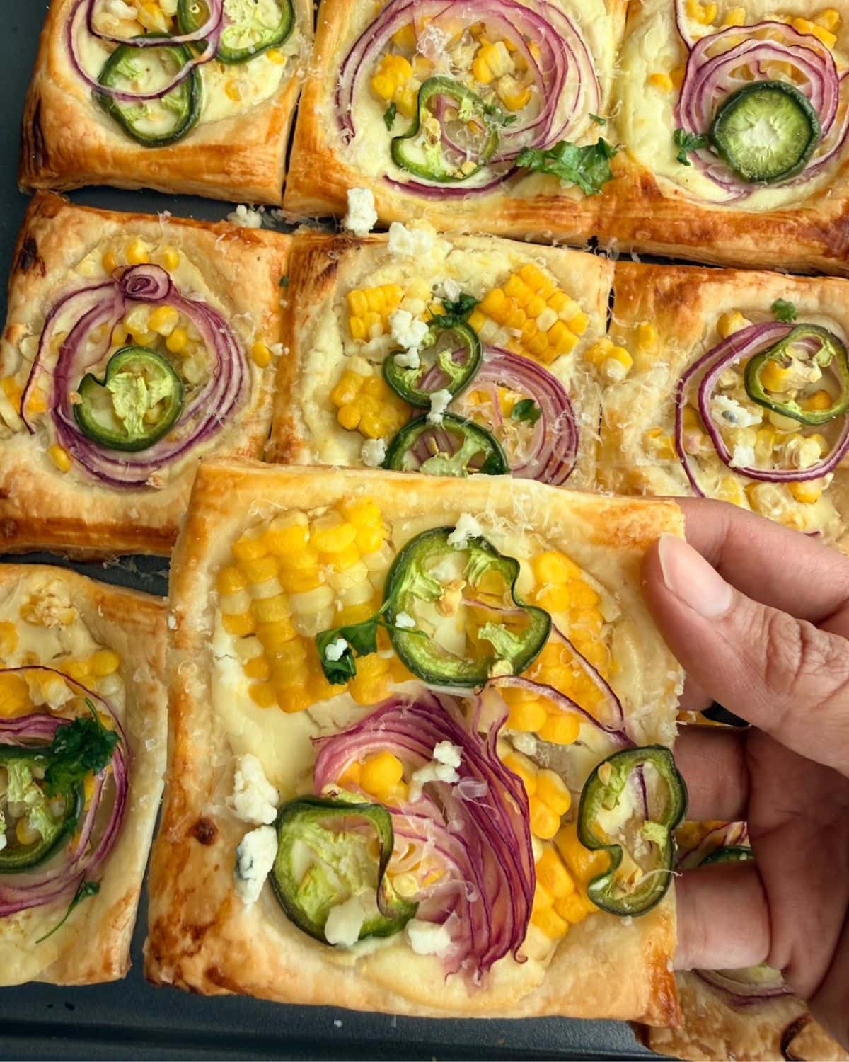 Lifting a square of baked corn puff pastry tart topped with feta and cilantro.