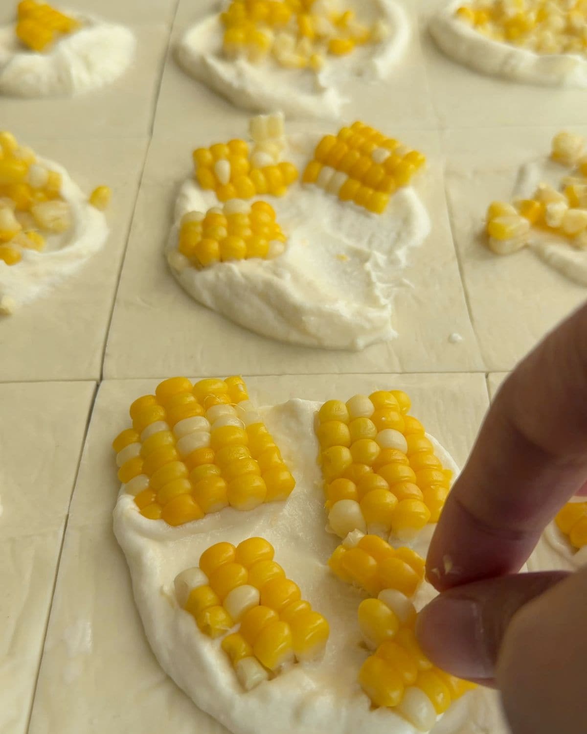 Overhead image showing corn being placed on dollop of ricotta for corn tart.