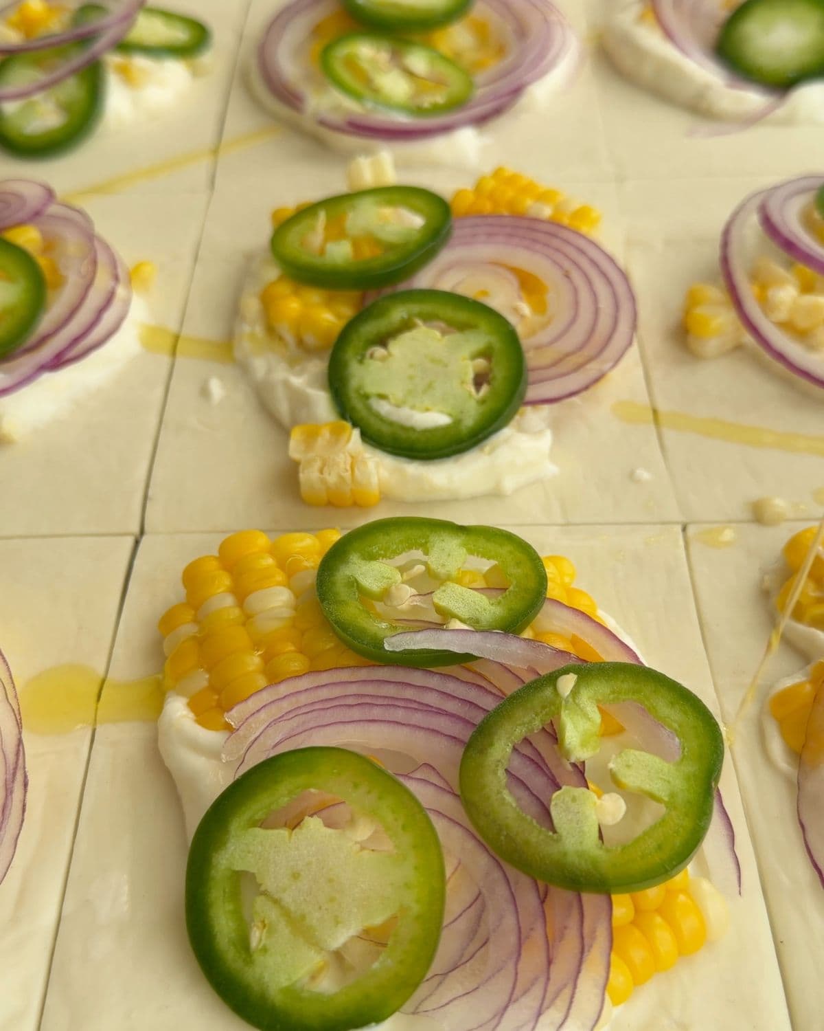 Overhead image showing jalapeno slices being placed on dollop of ricotta for corn tart.