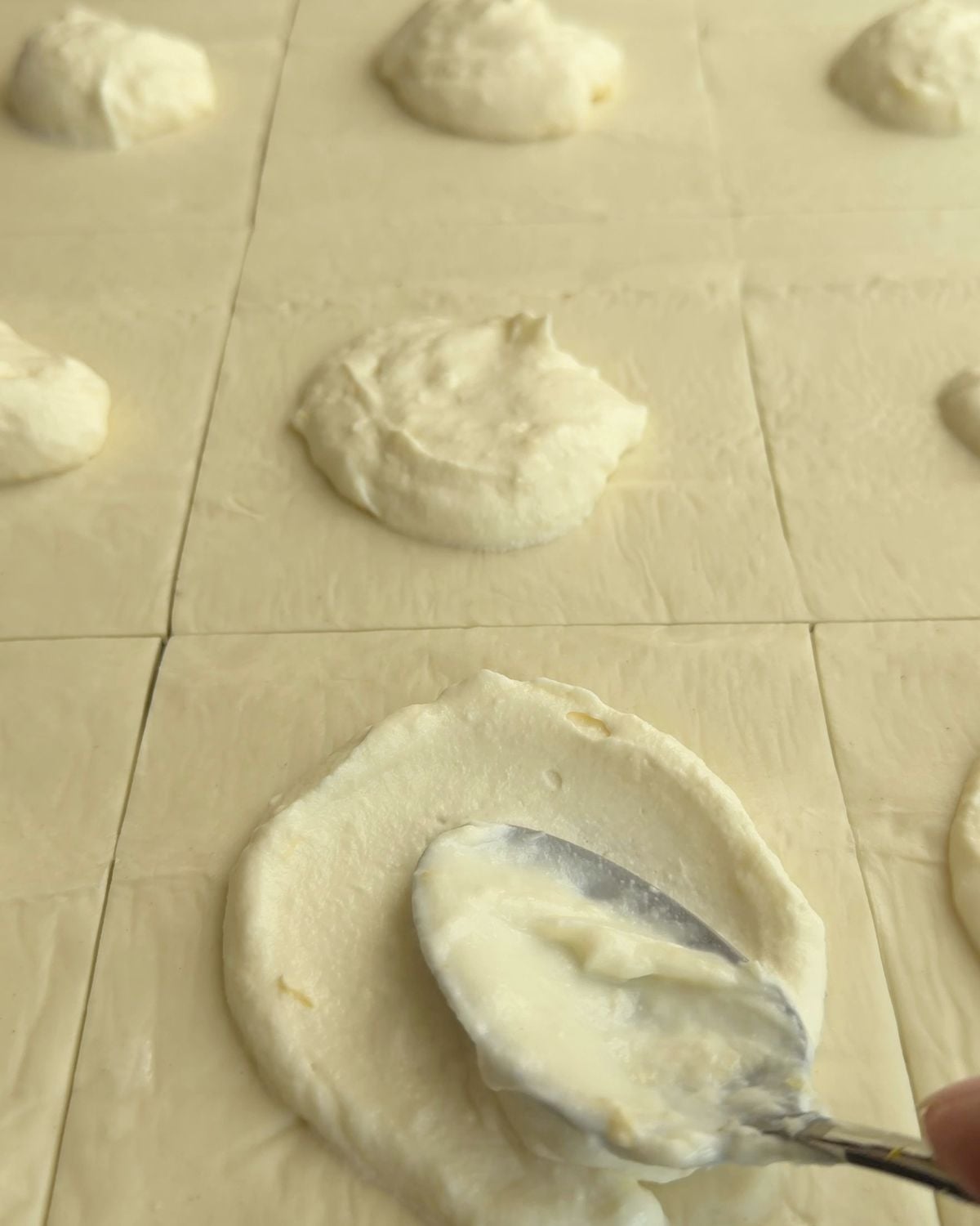 Spreading the ricotta mixture onto the scored puff pastry squares.