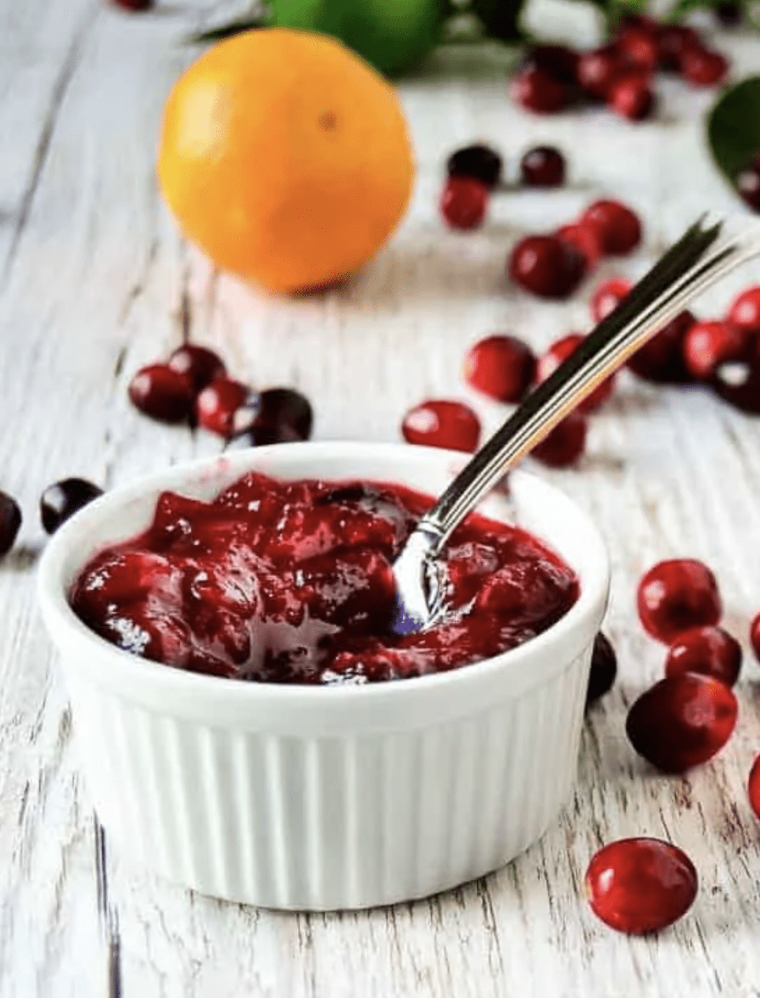 A straight view of cranberry orange sauce with fresh berries, orange and lime on the background.