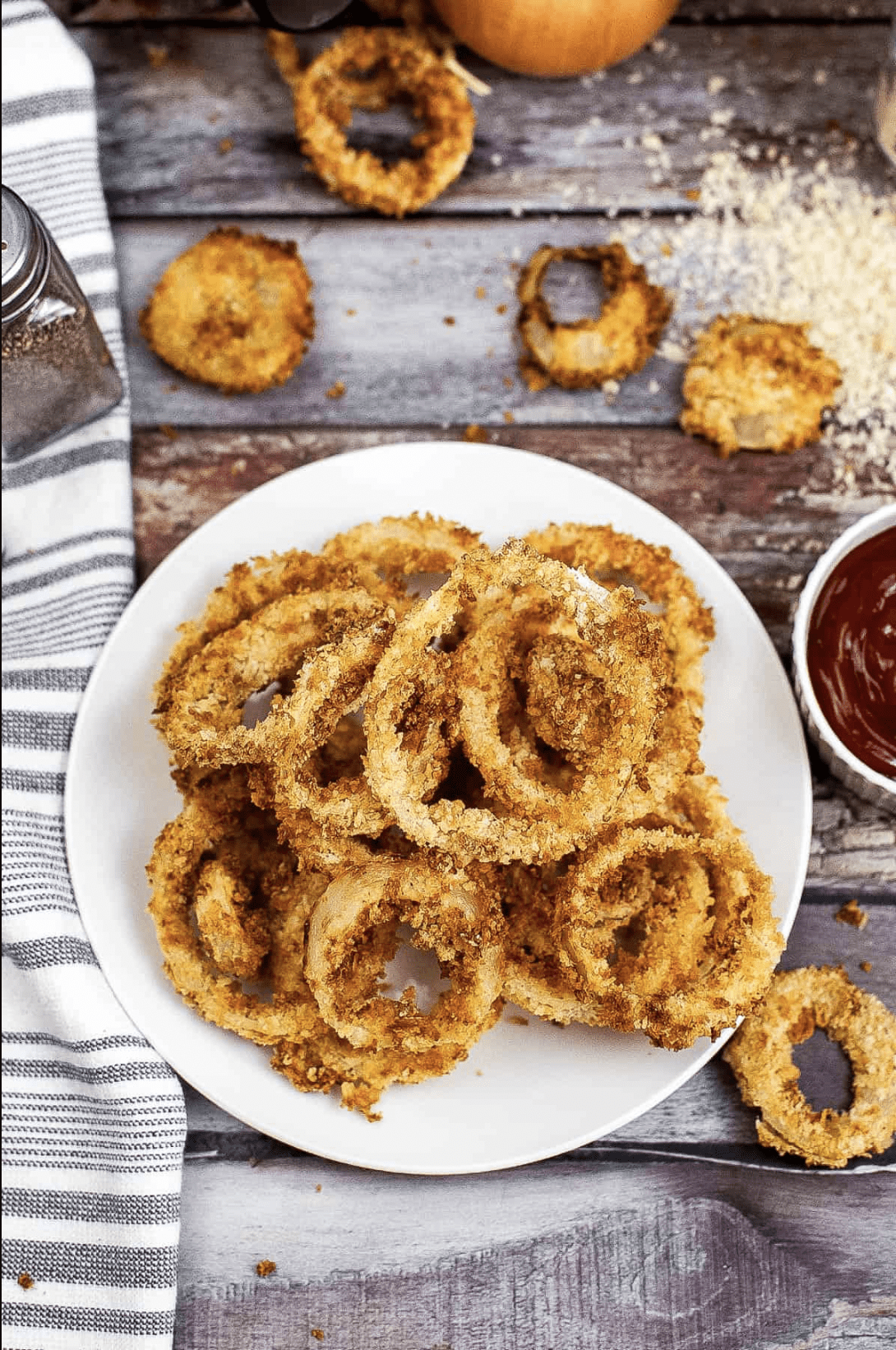 An overhead shot of air fryer onion rings on a plate served with tomato ketchup.