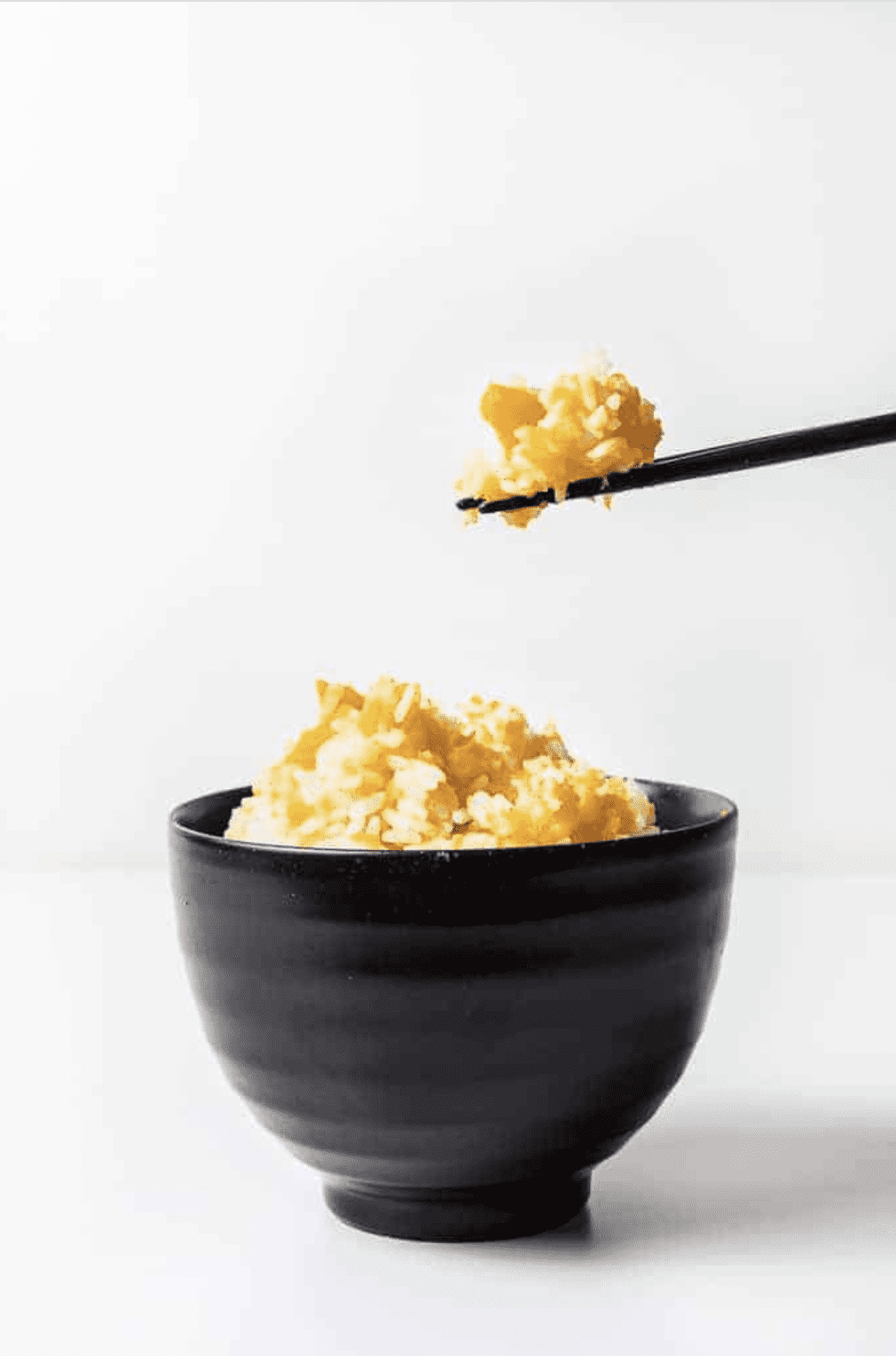 A straight view of instant pot kabocha squash rice in a black bowl with chopsticks takes the dish out.