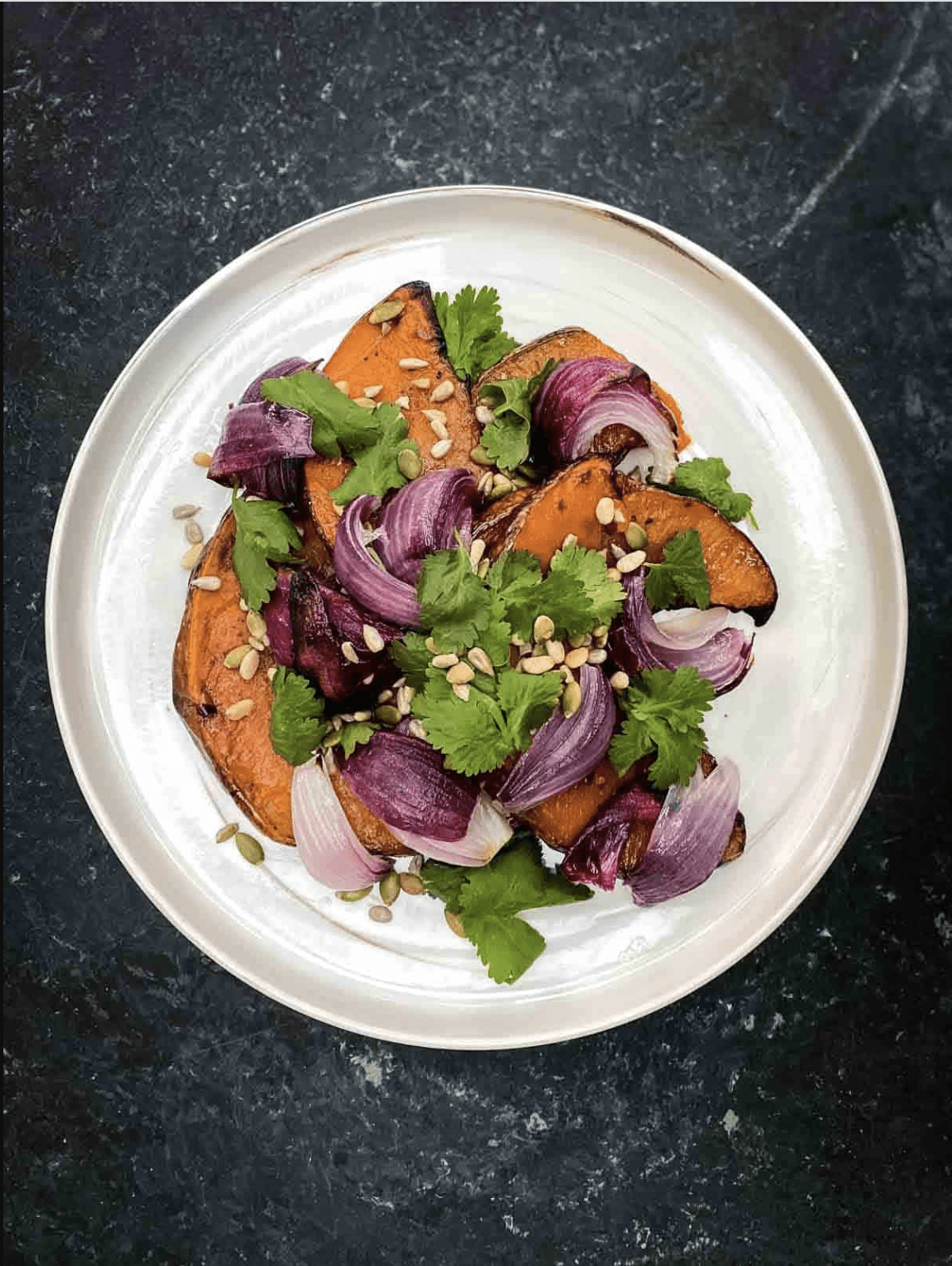An overhead view of roasted spiced kabocha squash salad placed on a white plate.
