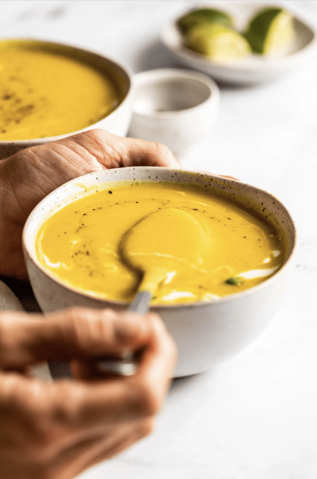 A straight shot of a hand lifting a spoonful of squash soup out of a dish.