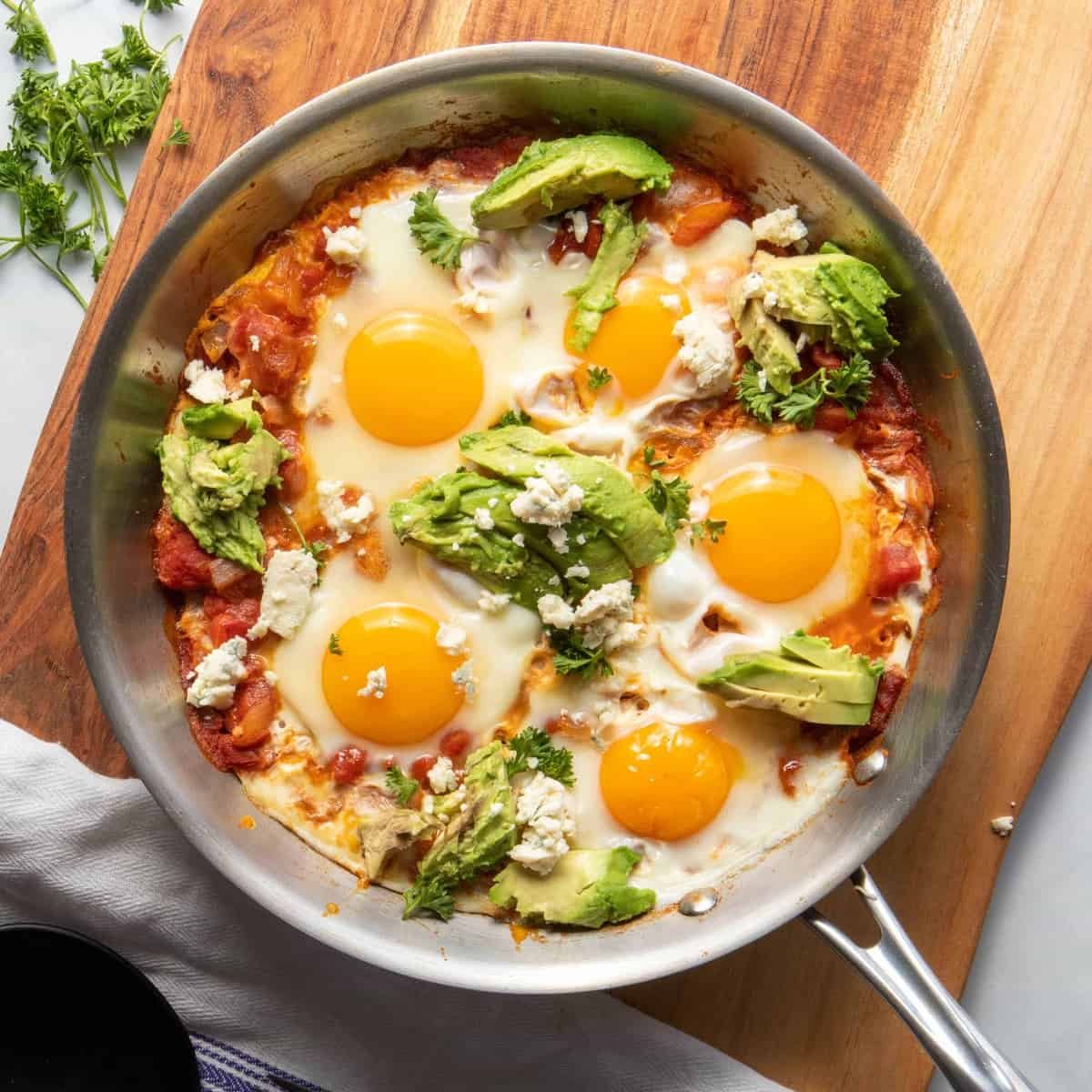 Delicious, Moroccan shakshuka with perfect runny yolk, garnished with parsley, avocado, and cheese