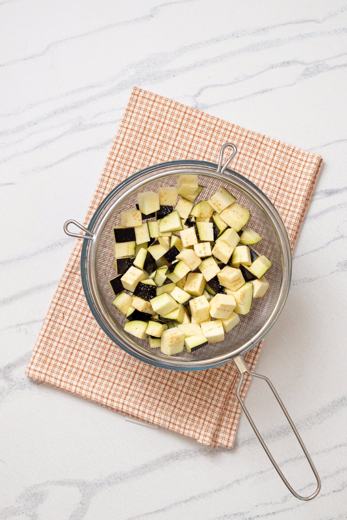 Cubed eggplant sprinkled with salt in a colander.